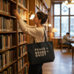 Woman in a library holding a tote bag with 'Peace = Books + Quiet' text.
